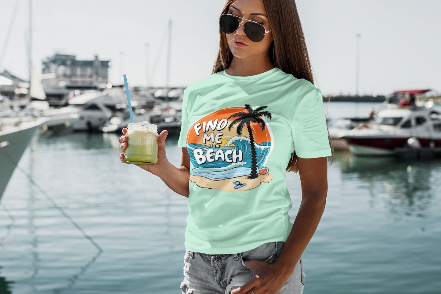 Woman holding a green smoothie wearing the Find Me at the Beach t-shirt near a marina