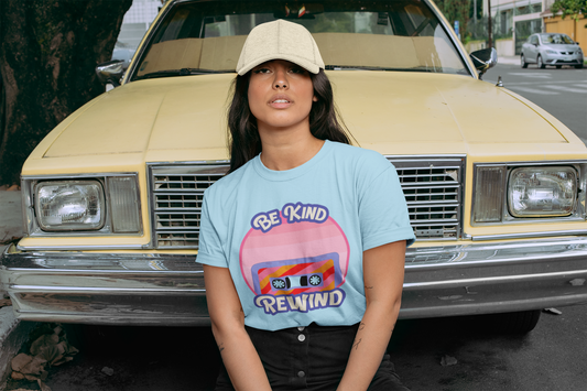 Woman wearing blue “Be Kind Rewind” t-shirt sitting on a retro yellow car