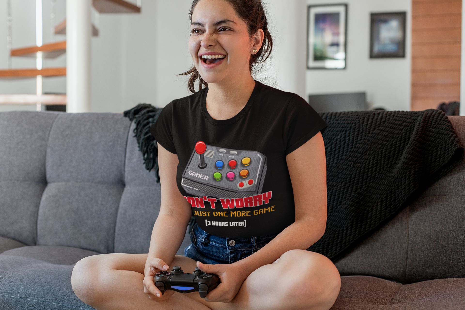 Woman laughing while playing video games in black "Just One More Game" T-shirt