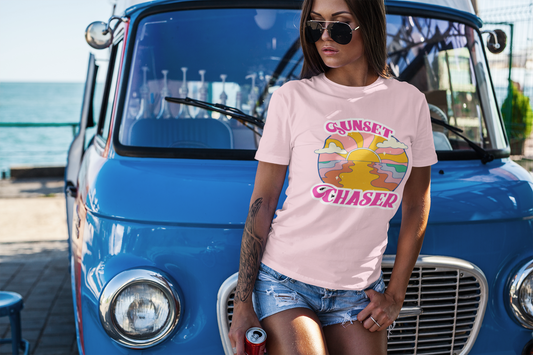 Woman wearing Sunset Chaser pink t-shirt standing near vintage blue van by the beach